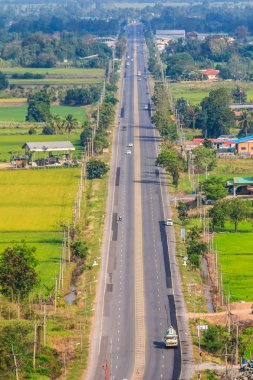 Havadan görünümü karayolu kırsal yeşil pirinç tarlaları ve mavi gökyüzü arka plan tepenin üzerinde. İl karayolu ile otomobil ve kamyon Phichit Eyaleti, Tayland Hills'te geçiş.