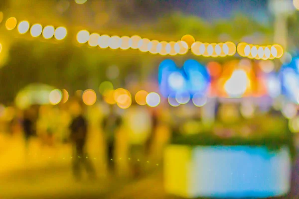 Blurred light with bokeh background of temple fair in Thailand. Walking street market with blurred people and bokeh light. Abstract blurred circular bokeh background.