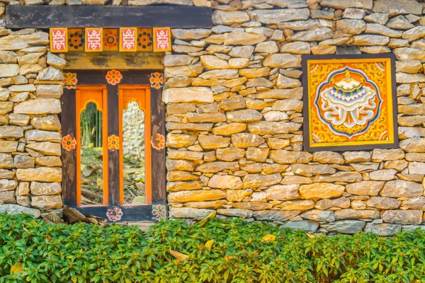 Bhutanese stone boundary wall with colorful carving wood artwork, green bush and copy space for your text. Bhutan style house decoration at the public park, Royal Flora Rajapruek, Chiang Mai, Thailand