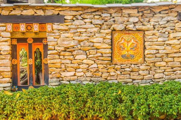 Bhutanese stone boundary wall with colorful carving wood artwork, green bush and copy space for your text. Bhutan style house decoration at the public park, Royal Flora Rajapruek, Chiang Mai, Thailand