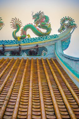 Güzel büyük yüz buruşturma ejderha Çin tapınaklarda dekoratif kiremit çatı üzerinde sürünerek. Geleneksel Çince Tapınağı ile ejderha heykeli mavi gökyüzü arka plan üzerinde renkli çatı detay. Seçici odak.