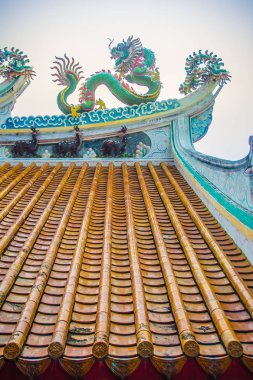 Güzel büyük yüz buruşturma ejderha Çin tapınaklarda dekoratif kiremit çatı üzerinde sürünerek. Geleneksel Çince Tapınağı ile ejderha heykeli mavi gökyüzü arka plan üzerinde renkli çatı detay. Seçici odak.