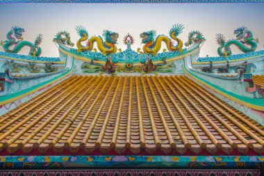 Güzel büyük yüz buruşturma ejderha Çin tapınaklarda dekoratif kiremit çatı üzerinde sürünerek. Geleneksel Çince Tapınağı ile ejderha heykeli mavi gökyüzü arka plan üzerinde renkli çatı detay. Seçici odak.