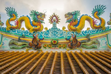 Güzel büyük yüz buruşturma ejderha Çin tapınaklarda dekoratif kiremit çatı üzerinde sürünerek. Geleneksel Çince Tapınağı ile ejderha heykeli mavi gökyüzü arka plan üzerinde renkli çatı detay. Seçici odak.