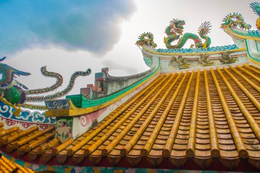 Güzel büyük yüz buruşturma ejderha Çin tapınaklarda dekoratif kiremit çatı üzerinde sürünerek. Geleneksel Çince Tapınağı ile ejderha heykeli mavi gökyüzü arka plan üzerinde renkli çatı detay. Seçici odak.