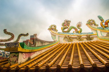 Güzel büyük yüz buruşturma ejderha Çin tapınaklarda dekoratif kiremit çatı üzerinde sürünerek. Geleneksel Çince Tapınağı ile ejderha heykeli mavi gökyüzü arka plan üzerinde renkli çatı detay. Seçici odak.