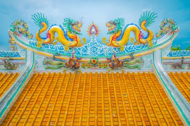 Güzel büyük yüz buruşturma ejderha Çin tapınaklarda dekoratif kiremit çatı üzerinde sürünerek. Geleneksel Çince Tapınağı ile ejderha heykeli mavi gökyüzü arka plan üzerinde renkli çatı detay. Seçici odak.