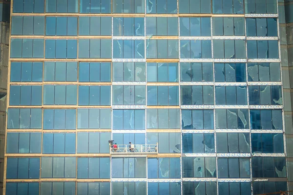 Construction workers on a suspended cradle platform on a skyscraper glass facade. Suspended cradle is similar to temporary suspended scaffolds for workers to work outside the skyscraper building.