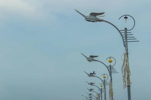 Row of the street lamps in bird shaped with the white clouds background. Perspective street lamps aligned with beautiful blue sky in background.