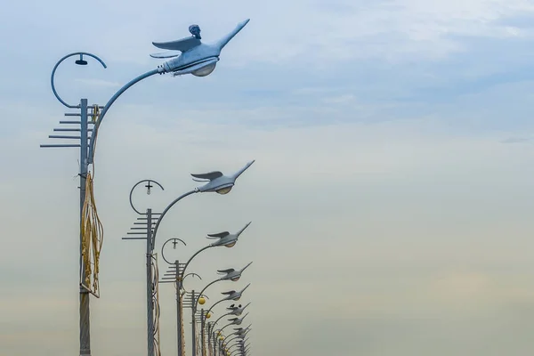 Row of the street lamps in bird shaped with the white clouds background. Perspective street lamps aligned with beautiful blue sky in background.
