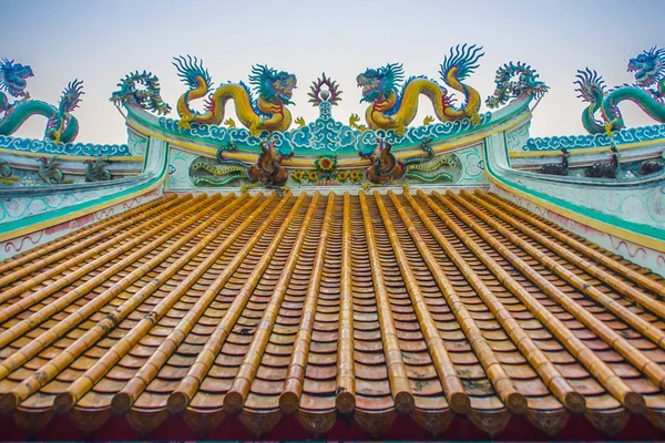 Güzel büyük yüz buruşturma ejderha Çin tapınaklarda dekoratif kiremit çatı üzerinde sürünerek. Geleneksel Çince Tapınağı ile ejderha heykeli mavi gökyüzü arka plan üzerinde renkli çatı detay. Seçici odak.