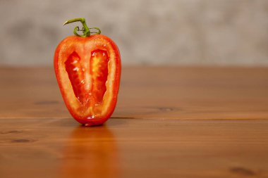 Dilimlenmiş kırmızı domates, ahşap bir masaya ve gri beton bir duvara karşı..