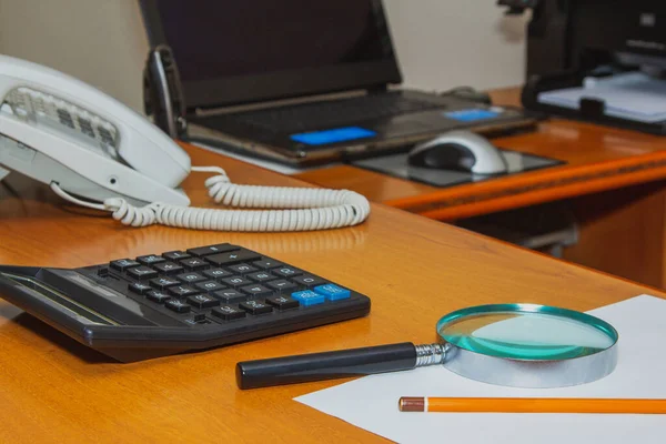 Masaüstü tahtasıyla büyüteç, hesap makinesi, telefon, kalem, çarşaf, arka plan bulanık dizüstü bilgisayar..