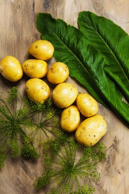 Patates, dereotu ve yaban turpu yaprağı, gri ahşap desenli arka planda taze sebzeler.