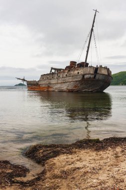 Eski bir ahşap Sovyet balina avcılığı teknesi, gemi körfez kıyısında karaya oturdu, ön planda deniz kıyısı, arka planda yarımadalar, Vityaz Körfezi,.