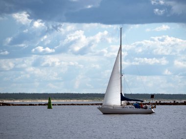 Yat nehir boyunca gider, güneşli bir gün ve anlamlı bulutlar. Arkaplanda kıyı çizgisi