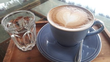 Kahverengi ahşap bir masaya yerleştirilmiş mavi seramik bir bardak üzerindeki kahve manzarası.. 