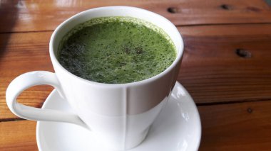 Kahverengi ahşap bir masaya seramik bir bardak üzerindeki yeşil çay manzarası..