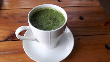 Kahverengi ahşap bir masaya seramik bir bardak üzerindeki yeşil çay manzarası..