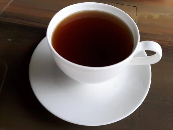 Top view of tea in a cup on a white ceramic coaster placed on a brown wooden table.
