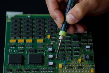 Erkeklerin elleri, yeşil elektronik bir tahtanın arka planında mikroçipli bir lehim makinesi tutuyor. Elektronik parçaların ve parçaların değiştirilmesi. Bilgisayar ekipmanları, endüstriyel ekipmanlar.