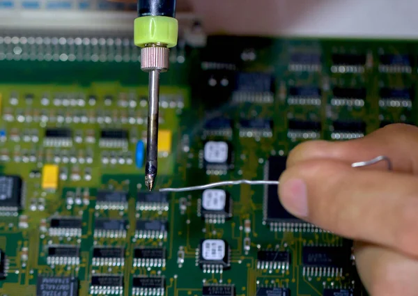 Erkek eller, elektronik bir tahtanın arka planına karşı lehim ve lehim tutarlar. Elektronik parçaların ve parçaların değiştirilmesi. Bilgisayar ekipmanları, endüstriyel ekipmanlar..