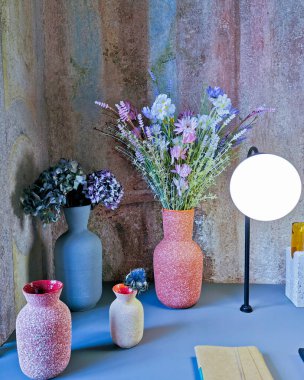 wild flowers and hydrangeas in stylish vases against a colored wall.design of a modern and stylish interior.two coral-pink vases, one the color of faded denim.vertical orientation. clipart