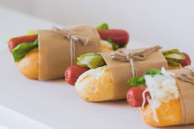 Üç tane ev yapımı sosisli, lahana, salatalık ve hafif ahşap bir arka planda taze yeşil salata. Ekolojik pakette Amerikan fast food 'u. Ulusal sosisli günü tatili..