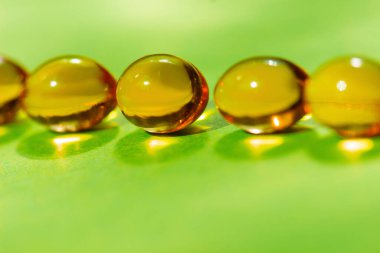 Yeşil zemin üzerinde bir sıra sarı kapsül. Yakın plan. Eksiklik kavramı veya vücudun sağlığı için aşırı vitamin tüketimi. Metin için alan.