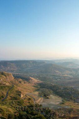 Yukarıdan bir italyan vadisini panoramik olarak görmek mümkün. Ağaçları ve odunları görmek mümkün. Arka planda yol ve dağ da var. Gün batımı anı