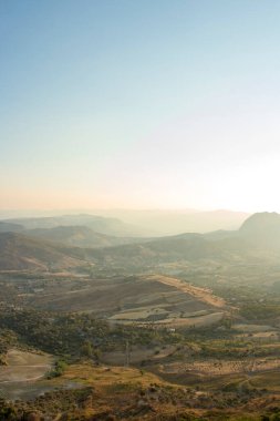 Yukarıdan bir italyan vadisini panoramik olarak görmek mümkün. Ağaçları ve odunları görmek mümkün. Arka planda yol ve dağ da var. Gün batımı anı