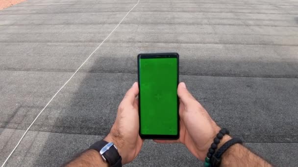 道路の緑のモックアップ画面スマートフォンの垂直方向の風景モードで見て若い男 インターネットの閲覧 動画の視聴 ブログ — ストック動画