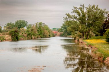 Gün batımında panoramik bir İtalyan bataklığı manzarası. Sarı ve turuncu çimenler, bir ahşap ve arka planda kırmızı bir ev. Gökyüzündeki bulutlar