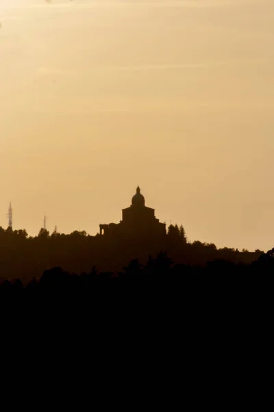 Gün batımında San Luca Sığınağı 'nın panoramik manzarası. Arka planda turuncu gökyüzü ve güneş var. Bolonya tepelerinin (colli bolognesi) odunu vardır. Emilia Romagna Bölgesi.