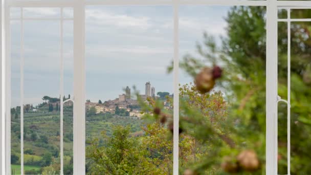 San Gimignano táj, mint látható egy fehér ablak, miközben a madarak repülnek. Ez látható a középkori falu a dombok a háttérben, vidék körülötte, és ciprusfa közelről. 
