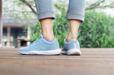 Mavi spor ayakkabılı ve kot pantolonlu kadın, su kenarındaki ahşap köprüde..