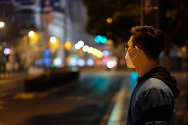 Şangay 'da koronavirüsü önlemek için yüz maskesi takan genç bir adamı kapatın. Renkli bokeh arkaplanı
