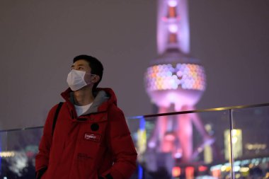 Koronavirüsü önlemek için yüz maskesi takan genç bir adam. Gece Şangay 'daki Doğu İnci TV Kulesi' ni bulanıklaştırdı. 