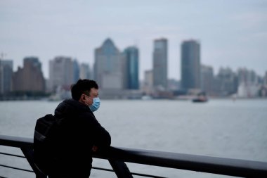 Şangay / Çin-2020: Coronavirus COVID-19 pnömoni birçok şehre yayılıyor. Cerrahi maske takan bir adam Çin 'deki sarmaşığa yaslanıyor.