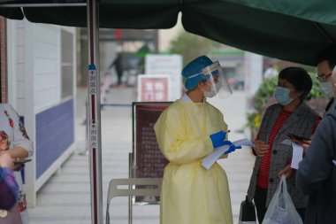 Şangay / Çin-Mayıs 2020: Doktor, Coronavirus 'tan kaçınmak için yüz maskesi ve giysi takarak hastanenin girişinde ziyaretçi sıcaklığını ölçüyor. İngilizce çevirisi 