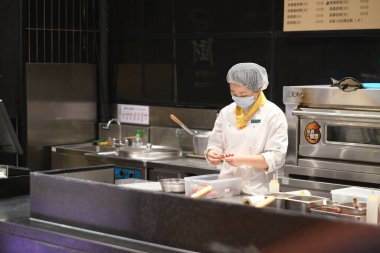 Şangay / Çin-Mayıs 2020: Bir kadın aşçı restoran mutfağında yemek hazırlıyor, covid-19 Coronavirus 'tan kaçınmak için maske takıyor.