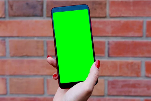 woman\'s hand showing green screen smartphone. Blur red bricks wall background