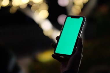 Karanlıkta yeşil ekranlı telefonu tutarak bir elinizi kapatın. Altın bokeh arkaplanı