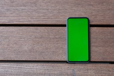 Eski ahşap masadaki yeşil ekran akıllı telefonun üst görüntüsü