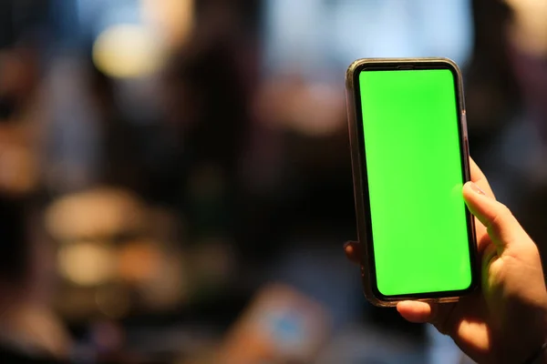 Bir elinle yeşil ekran akıllı telefonu tıkla. Bulanık bokeh arkaplanı