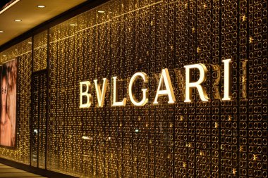 Şangay / Çin-Temmuz 2019: Altın parlayan Bvlgari 'nin büyük logosu geceleri mağazanın dışındaki duvarda. İtalyan lüks markası. Bulanık reklam panosu. Bakış açısı