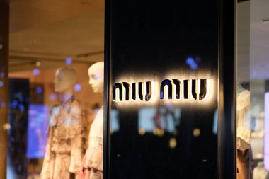 Şangay / Çin-Temmuz 2019: Karanlık arka planda aydınlatılmış miu miu logosunu kapatın. Odaklanamayan plastik modeller ve giysi ürünleri mağazada. İtalyan moda kadın kıyafetleri ve aksesuar markası.
