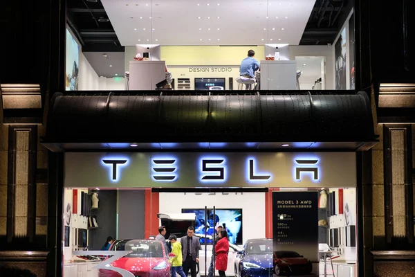 Şangay / Çin-Ekim 2019: Geceleri TESLA mağazasının cephesi. Dükkan tabelasında parlak TESLA logosu. Müşteriler ve satıcı içeride.