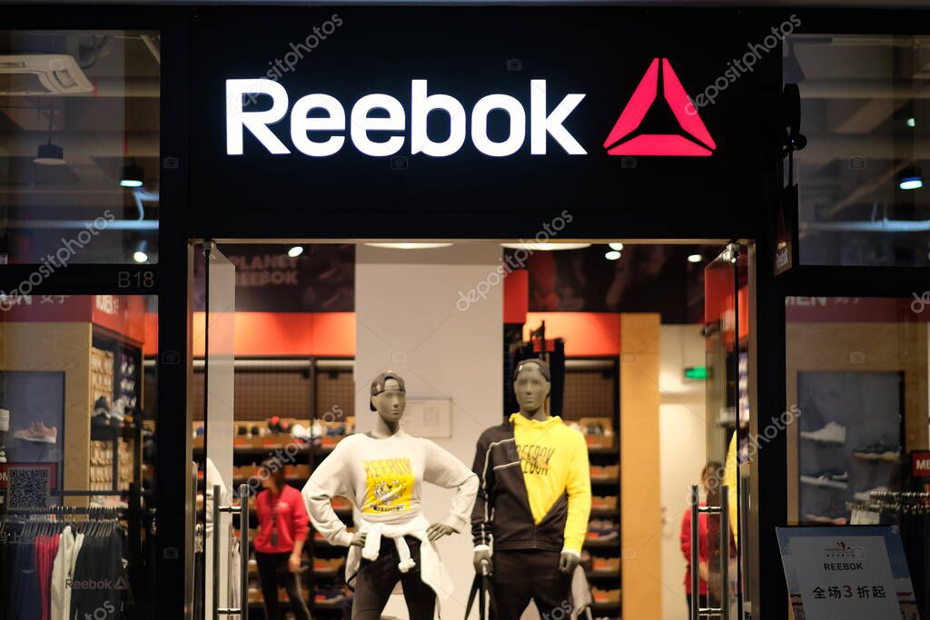Shanghai/China-Oct.2019: facade of Reebok clothing store in Florentia Village Outlets. White brand logo.Illuminated clothing store inside. An American sports brand.