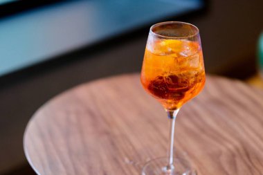 İçinde buz küpleri olan turuncu renkli bir şarap bardağını ahşap masanın üzerine koy. Bulanık arkaplan